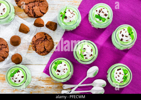 mint Cheesecake Mousse Dessert topped with whipped cream and chocolate chips in glass cups with chocolate cookies, and homemade truffles on background Stock Photo