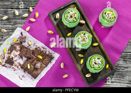 pistachio nut Cheesecake Mousse Dessert topped with whipped cream and chocolate chips in glass cups on dark wooden board.  chocolate bar cut in pieces Stock Photo