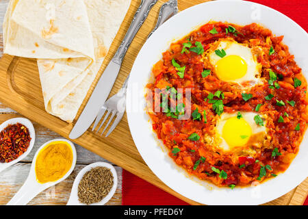 shakshuka - liquid egg yolks,bell pepper, chili, tomato sauce and spices on white dish with flatbread on chopping board. cumin, curcuma, pepper flakes Stock Photo