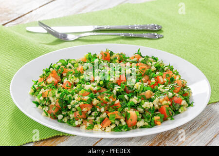 Tabbouleh parsley salad on white platter on table mat with fork and knife on background, view from above, close-up Stock Photo