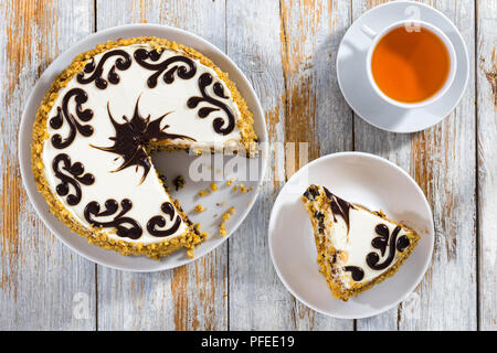 delicious sponge cake with honey and prunes decorated with smooth shiny chocolate frosting, cut in slices, on old dark wooden planks with cup of black Stock Photo