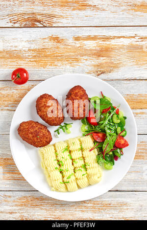 delicious hot mashed potato sprinkled with greens, juicy meat cutlets and fresh healthy salad on white plate on old rustic boards, vertical view from  Stock Photo