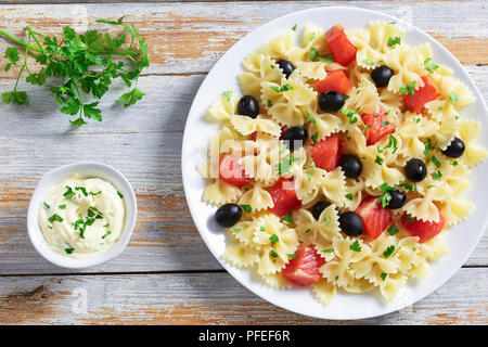 delicious italian pasta Farfalle with Smoked Salmon, black olives sprinkled with parsley on white plate on old wooden table with cream sauce and spice Stock Photo