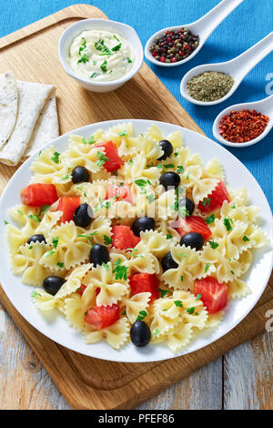 delicious italian pasta Farfalle with Smoked Salmon, black olives sprinkled with parsley on white plate on chopping board with cream sauce and spices  Stock Photo