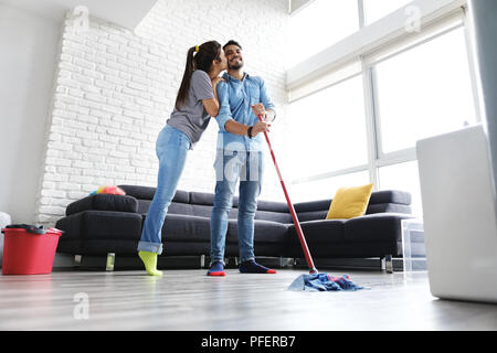 Young couple doing housework and chores. Man and girlfriend wipes the floor with mop. The woman feels proud of her husband and kisses him. Stock Photo