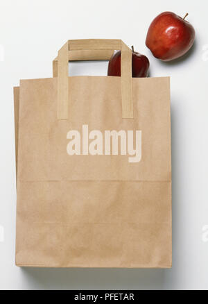 Brown paper bag with two red apples falling out, side view Stock Photo