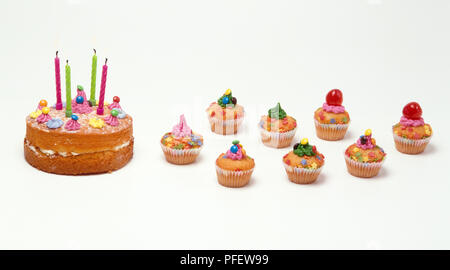 Birthday cake with candles next to decorated cupcakes Stock Photo
