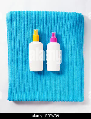 Two white plastic bottles with coloured lids lying on folded ribbed bath towel. Stock Photo