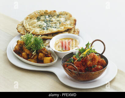 Bowls of prawns cooked in tomatoes (Kadhhai Jhinga), lentil curry (Tadka Dal), paneer and baby corn with ginger, and stack of flat bread, arranged on a serving dish Stock Photo