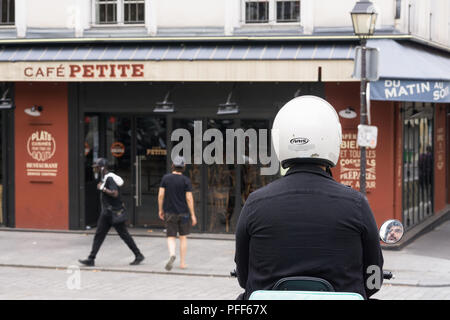 Street scene in Paris - motorist on scooter and two pedestrians near the Cafe Petit in the 10th arrondissement of Paris, France, Europe. Stock Photo