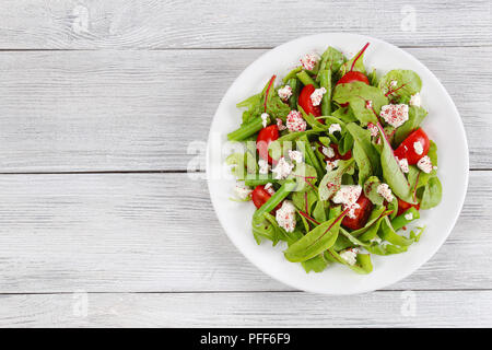 delicious healthy low calories salad of green beans, chard, arugula, tomatoes and cottage cheese, sprinkled with sumac on white plate, on wooden table Stock Photo
