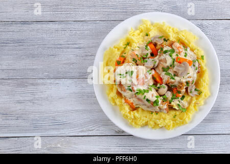 delicious Rabbit legs braised in sour cream with mushrooms and carrots served with mashed potatoes on white plate on wooden boards, view from above Stock Photo