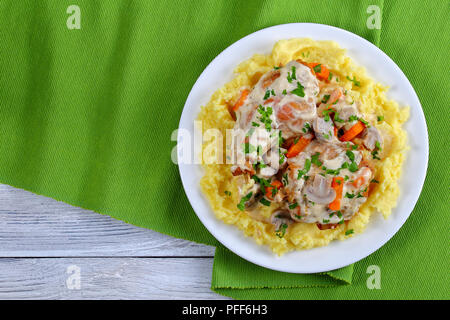 delicious Rabbit braised in sour cream with mushrooms and carrots served with mashed potatoes on white plate on green table mat, view from above Stock Photo
