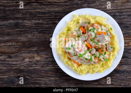 delicious Rabbit braised in sour cream with mushrooms and carrots served with mashed potatoes on white plate on dark wooden table, view from above Stock Photo