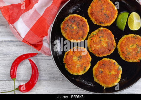 delicious fresh fried homemade fish cakes with mashed potato on skillet with lime slices, on wooden table with kitchen towel, chili peppers, authentic Stock Photo