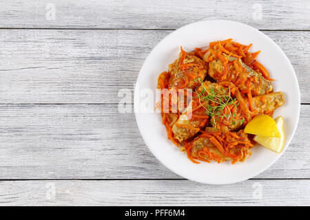 delicious Notothenia or cod icefishes stewed with carrot and onion, spices and herbs served on white plate with lemon wedges, view from above Stock Photo