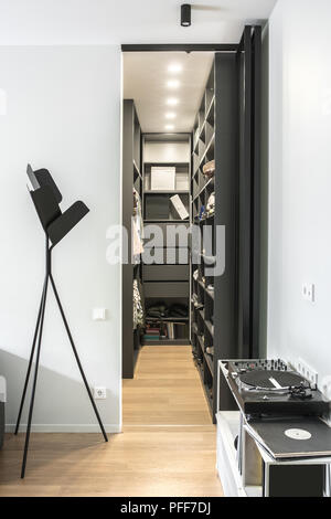 Room in a modern style with light walls and a parquet on the floor. There is luminous black wardrobe with shelves and drawers with clothes and shoes a Stock Photo