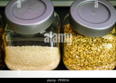 Various raw cereals, grains, beans and pasta for healthy cooking in glass jars on kitchen shelf, white background. Clean eating, vegetarian, vegan, ba Stock Photo