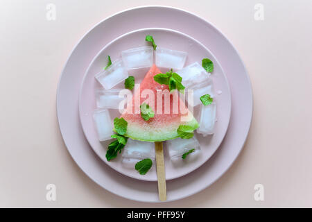 Frozen watermelon popsicles – homemade ice cream with mint on pink plate. Top view Stock Photo