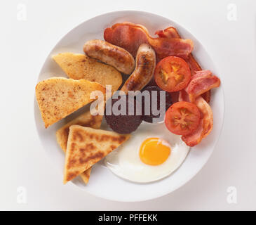 Ulster Fry, breakfast plate including sausages, bacon, black pudding, fried egg, tomatoes and bread, view from above. Stock Photo