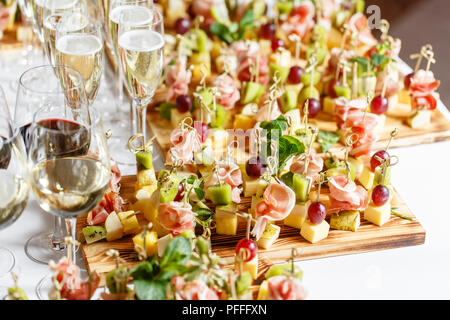 solemn happy new year banquet. Lot of glasses champagne or wine on the table in restaurant. buffet table with lots of delicious snacks. canapes, bruschetta, and little desserts on wooden plate board Stock Photo