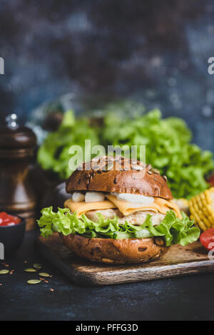 Tasty Chicken Burger With Cheese, Sauce, Lettuce On Wooden Serving Board. Closeup view, Selective focus Stock Photo