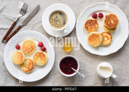 Breakfast Table Cottage Cheese Pancakes, Coffee, Cream, Honey and Jam. Textile background. Tasty Breakfast, Syrniki. Russian Cuisine Stock Photo