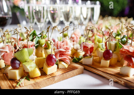 solemn happy new year banquet. Lot of glasses champagne or wine on the table in restaurant. buffet table with lots of delicious snacks. canapes, bruschetta, and little desserts on wooden plate board Stock Photo