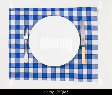 White plate on a check mat with a silver fork and bone-handled knife, overhead view. Stock Photo