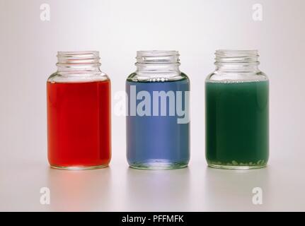 Three jars containing red cabbage juice, turned red by adding lemon (acid), green by adding soap (alkali), and blue with nothing added Stock Photo