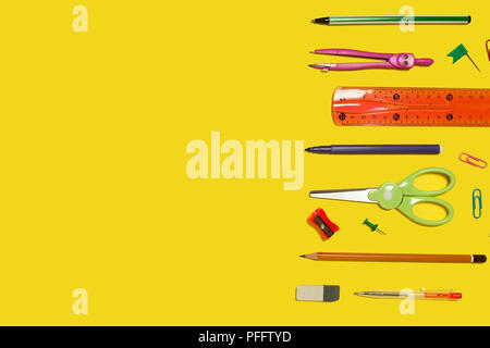 row of different school and office stationary and gadgets lying on a yellow background. free space for advertising text Stock Photo