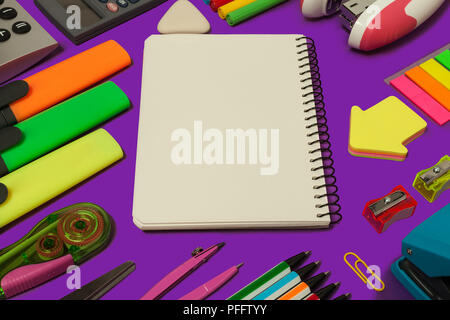 various stationary surrounding an opened notebook lying on a purple background. concept of office and educational chancery Stock Photo