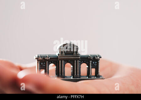 a miniature of the Puerta de Alcala in Madrid, Spain, on the hand of a young man against an off-white background, with some blank space on top Stock Photo