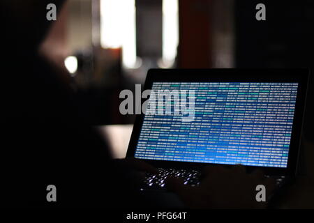 Computer Hacker silhouette typing on computer in a dark room. Working on blue binary code technology. binary data, computer programming and network Stock Photo