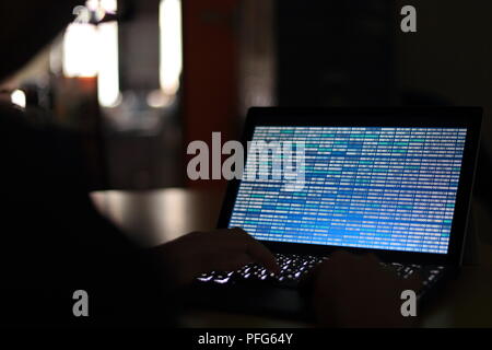 Computer Hacker silhouette typing on computer in a dark room. Working on blue binary code technology. binary data, computer programming and network Stock Photo