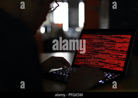 Computer Hacker silhouette typing on computer in a dark room. Working on binary code technology. binary data, computer crime and network security Stock Photo