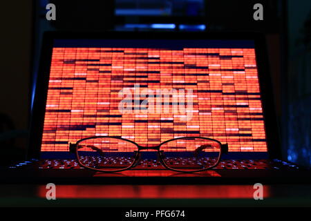 Data crisis and computer crime. glasses in front of computer notebook with red binary code in a dark room. technology, binary data, computer crime Stock Photo