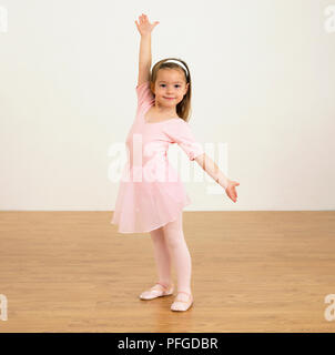 Girl in ballerina outfit holding one arm up and the other to her left, 5 years old Stock Photo