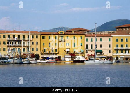 Italy, Tuscany, Elba, Portoferraio, boats in harbour, orange and pink palazzi on harbourside, mountains in background. Stock Photo