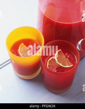 Red drink in a glass jug and served in two glasses with slices of lemon, high angle view Stock Photo