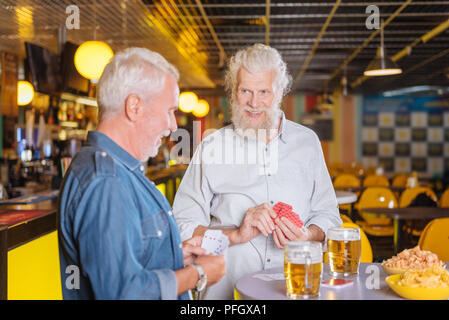 Delighted aged men playing card games and drinking Stock Photo