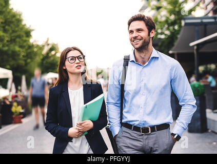 A young businessman and businesswoman walking on a sidewalk, talking. Stock Photo