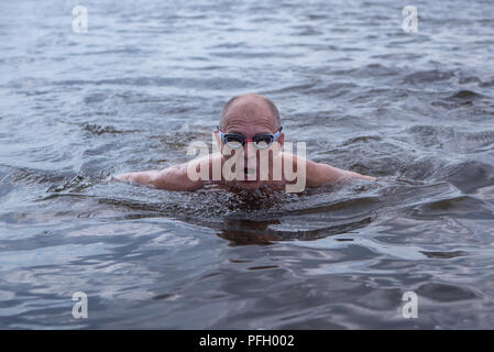 An elderly muscular man in swimming goggles swims with a butterfly style, front view Stock Photo