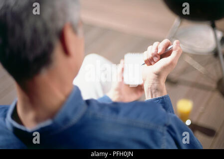 Back of head of mature man in blue shirt sitting, clicking a pen in one hand, holding pad of paper in one hand, close-up from behind. Stock Photo