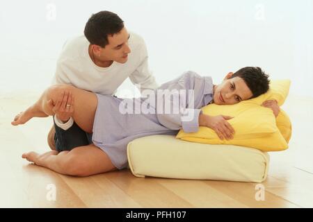 Woman in labour lying on cushion, man crouching by her side and holding her leg for support Stock Photo