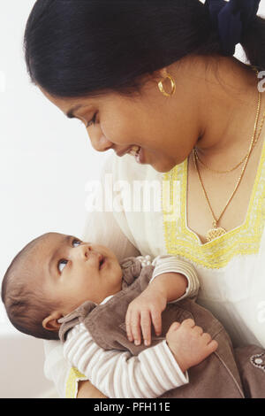 Black-haired woman cradling baby, looking at each other Stock Photo