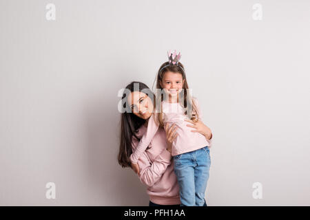 A small girl with crown headband standing on a a stool in front of her mother. A studio shot on a white background. Stock Photo