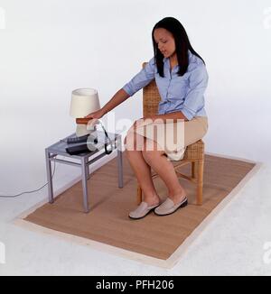 Woman sat on chair putting receiver back towards phone Stock Photo