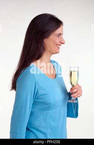 Woman in blue top holding a glass of champagne, looking away, smiling Stock Photo