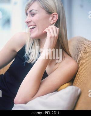 Sitting blonde woman laughing and playing with her hair, side view. Stock Photo
